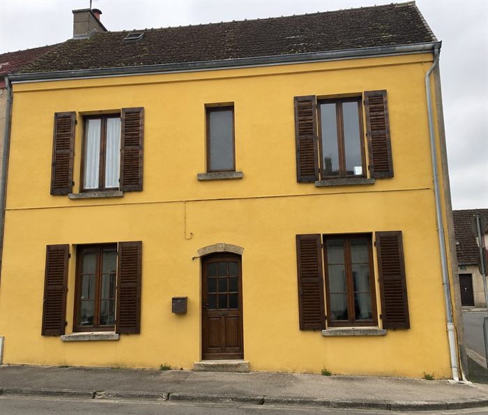 Façade de maison repeinte en jaune, volets marron conservés